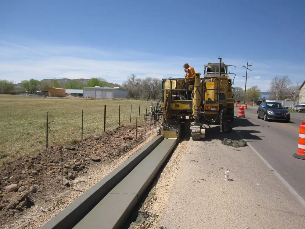 A B Hansen Construction slipform machine extruding new concrete curb and gutter along a rural road